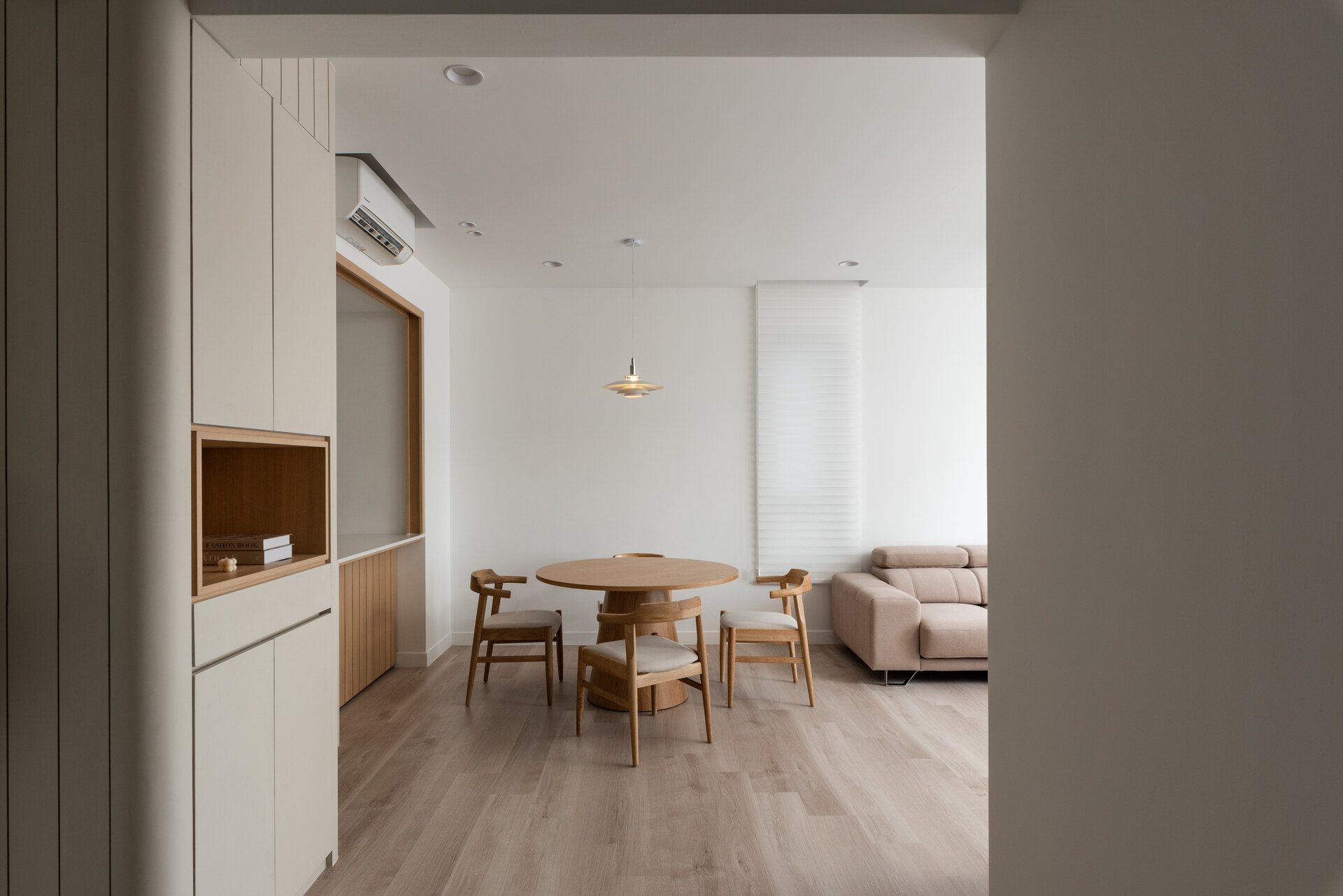 Minimalist dining room with wooden round table and chairs, featuring light wood flooring and neutral tones in an Alam Damai apartment